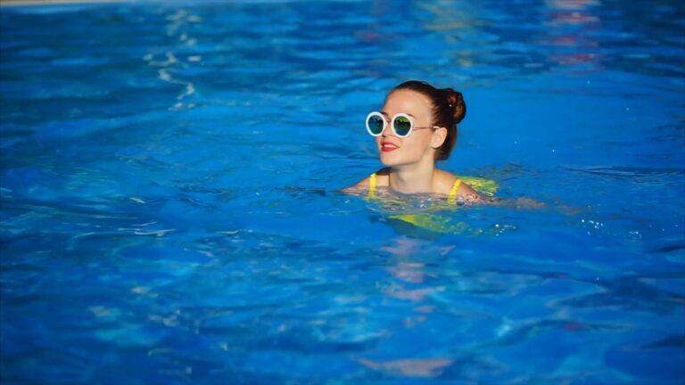 A stylish and joyful girl in fashionable glasses swims in an outdoor pool on a hot [HD]
